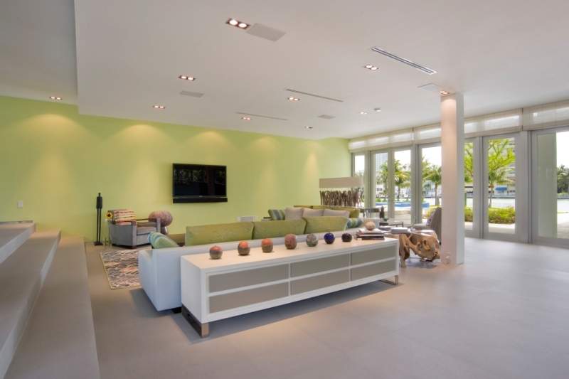 Open, indoor living area with couches, chairs in shades of gray and white. One light green accent wall.