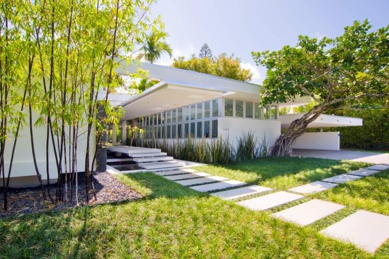 White exterior of Glass House, with large pavers leading to steps surrounded by liriope plants and bamboo.